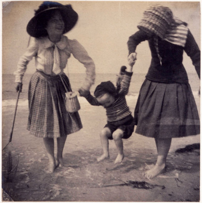 Two girls paddling in the sea, swinging little Madeleine. Photograph taken at Perros-Guirec in Brittany, 1909