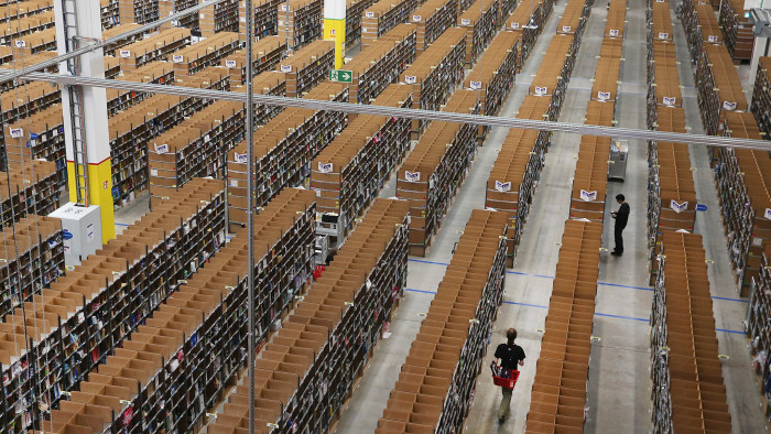 Workers walk among shelves lined with goods at an Amazon warehouse on September 4, 2014 in Brieselang, Germany