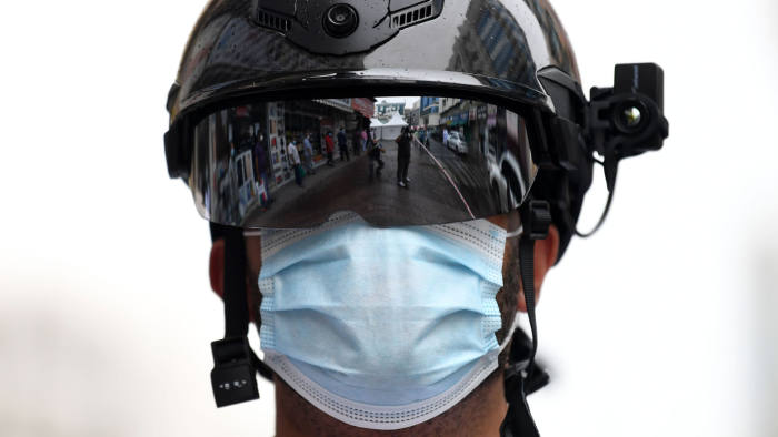Foreign workers standing in line as they wait to be checked for the novel coronavirus at a testing centre in the Naif area of the Gulf Emirate of Dubai, are reflected against the helmet of a policeman, on April 15, 2020. (Photo by KARIM SAHIB / AFP) (Photo by KARIM SAHIB/AFP via Getty Images)
