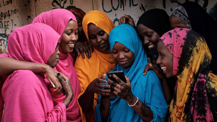 TOPSHOT - Young Somali refugee women look at a smartphone as they stand together at Dadaab refugee complex, in the north-east of Kenya, on April 16, 2018. - The Dadaab refugee complex which has some 235269 refugees and asylum seekers in four camps about 80kms from the Somali-Kenyan border was established in 1991, according to UNHCR camp population statistics in January 2018. (Photo by Yasuyoshi CHIBA / AFP) (Photo credit should read YASUYOSHI CHIBA/AFP via Getty Images)