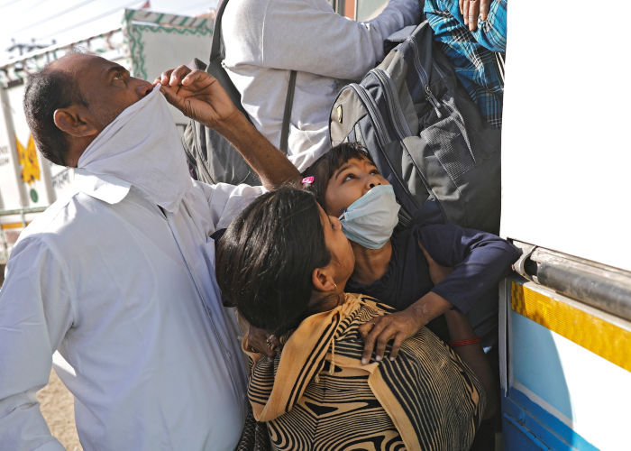 On the outskirts of New Delhi on March 29, a woman pushes her daughter on to an overcrowded bus as they attempt the journey back to their home village