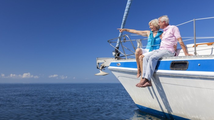 A happy senior couple sitting on the side of a sail boat on a calm blue sea looking and pointing to a clear horizon