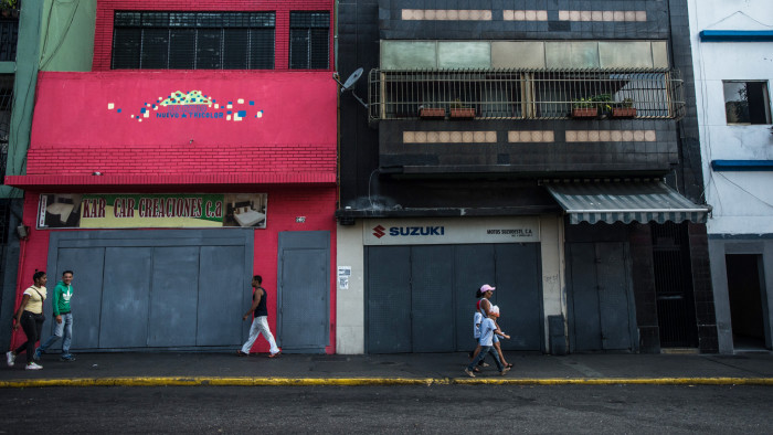 People walk past a row of closed stores in the usually busy downtown shopping district in Caracas, Venezuela, on Tuesday, March 22, 2016. Venezuela shut down for a week as the government struggles with a deepening electricity crisis. The government has rationed electricity and water supplies across the country for months and urged citizens to avoid waste as Venezuela endures a prolonged drought that has slashed output at hydroelectric dams. Photographer: Meridith Kohut/Bloomberg