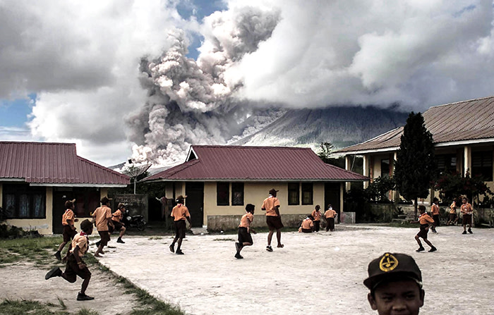 -- AFP PICTURES OF THE YEAR 2017 -- Elementary school children play outside of their classrooms as mount Sinabung volcano spews thick volcanic ash as seen from Karo, North Sumatra province, on February 10, 2017. Many residents in the area have been forced to relocate to other villages of Northern Sumatra at a safer distance from mount Sinabung volcano, one of the most active in Indonesia. / AFP PHOTO / STRSTR/AFP/Getty Images