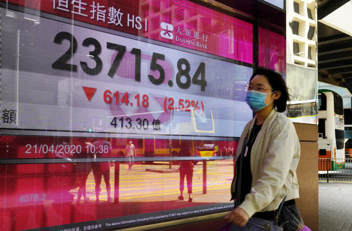 A woman wearing face mask walks past a bank electronic board showing the Hong Kong share index at Hong Kong Stock Exchange Tuesday, April 21, 2020. Asian shares skidded on Tuesday after U.S. oil futures plunged below zero as storage for crude runs close to full amid a worldwide glut as demand collapses due to the pandemic. (AP Photo/Vincent Yu)