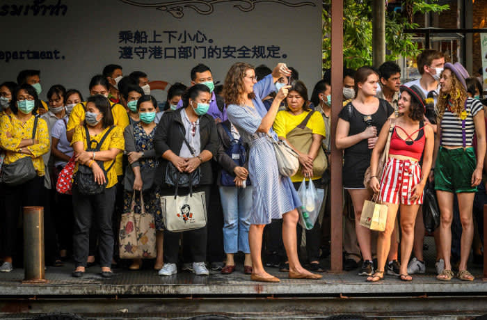 TOPSHOT - Tourists take pictures next to commuters with facemasks, worn amid fears of the spread of the COVID-19 novel coronavirus, as they wait for a canal boat in Bangkok on March 2, 2020. - A Thai man has died from complications doctors say were due to the deadly coronavirus, though health officials were reluctant on March 2 to conclusively confirm the cause of his death. (Photo by Mladen ANTONOV / AFP) (Photo by MLADEN ANTONOV/AFP via Getty Images)