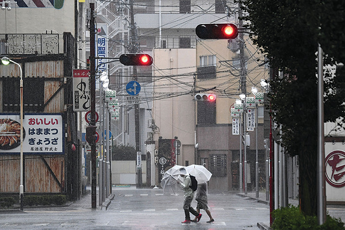 TOPSHOT - Pedestrians cross a street in Hamamatsu, Shizuoka prefecture on October 12, 2019, ahead of Typhoon Hagibis' expected landfall in central or eastern Japan later in the evening. - Powerful Typhoon Hagibis on October 12 claimed its first victim even before making landfall, as Japanese weather authorities issued a top-level emergency rain warning and millions were issued non-compulsory evacuation orders. (Photo by Anne-Christine POUJOULAT / AFP) (Photo by ANNE-CHRISTINE POUJOULAT/AFP via Getty Images)