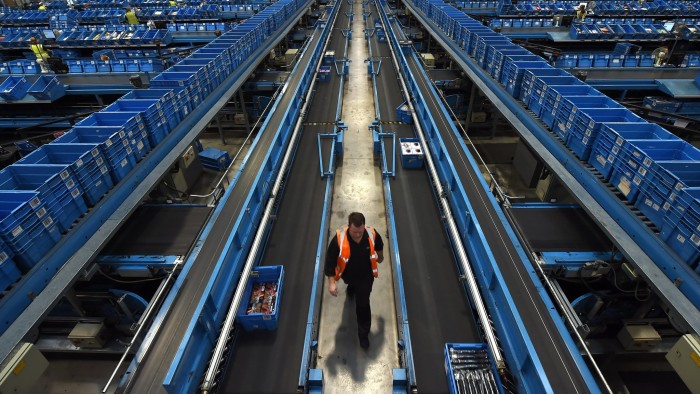 A worker walks alongside a conveyor belt as items are sorted into crates to be sent to retail stores from the Argos Distribution Centre in Burton-upon-Trent, central England, on November 27, 2015.