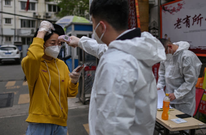 A man wearing a protective suit checks a woman's temperature next to a residential area in Wuhan, in China's central Hubei province on April 7, 2020. - Wuhan, the central Chinese city where the coronavirus first emerged last year, partly reopened on March 28 after more than two months of near total isolation for its population of 11 million. (Photo by Hector RETAMAL / AFP) (Photo by HECTOR RETAMAL/AFP via Getty Images)