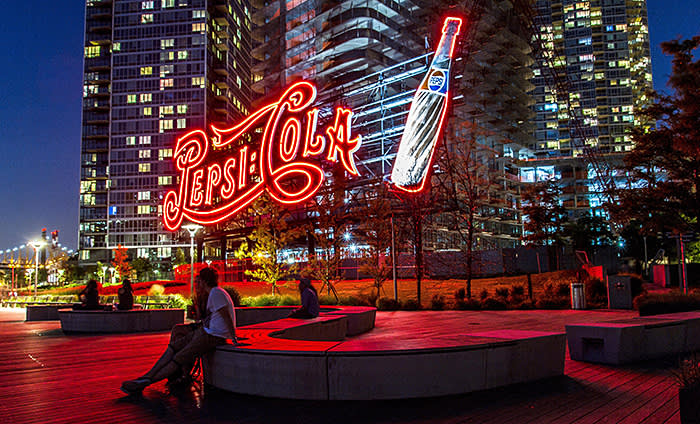 F1A7N5 Couple sitting bathed in red light from the Giant neon Pepsi Cola sign ,Gantry Plaza State Park, Long Island City NY