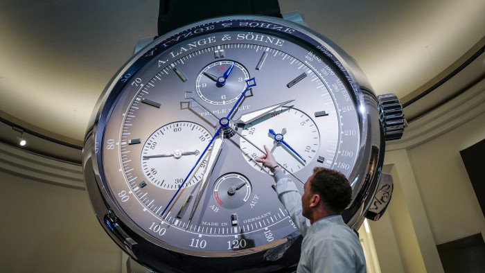 A staff gestures next to a giant watch at the stand of German watchmaker A. Lange