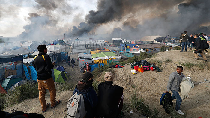 Smoke rises the sky as migrants and journalists look at burning makeshift shelters and tents in the &quot;Jungle&quot; on the third day of their evacuation and transfer to reception centers in France, as part of the dismantlement of the camp in Calais, France, October 26, 2016.          REUTERS/Philippe Wojazer TPX IMAGES OF THE DAY - LR1ECAQ0UA87V