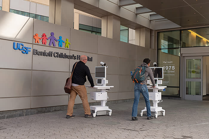Two staff members wheel Amwell telemedicine carts into the entrance of the University of California San Francisco (UCSF) Benioff Children's Hospital in Mission Bay, San Francisco, California during an outbreak of the COVID-19 coronavirus, March 16, 2020. As a result of the outbreak, patients are increasingly being asked to conduct telemedicine appointments to avoid infecting healthcare workers. (Photo by Smith Collection/Gado/Getty Images)