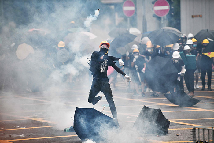 TOPSHOT - A protester throws tear gas back at police officers during a demonstration in the district of Yuen Long in Hong Kong on July 27, 2019. - Riot police fired tear gas at protesters marching through a Hong Kong town near the Chinese border to rally against suspected triad gangs who beat up pro-democracy demonstrators there last weekend. (Photo by Anthony WALLACE / AFP) (Photo credit should read ANTHONY WALLACE/AFP/Getty Images)