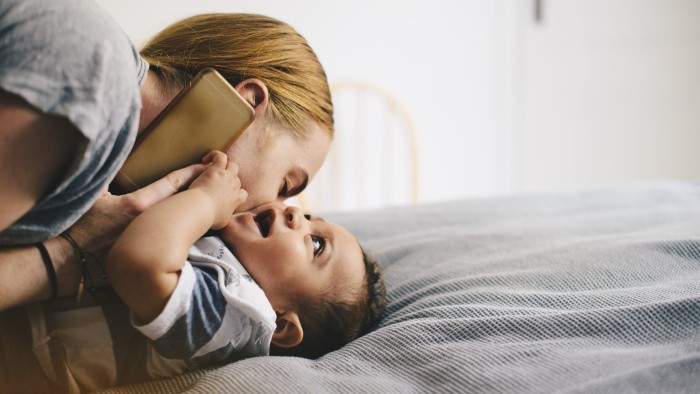 Mother kissing son while talking on mobile phone at bed