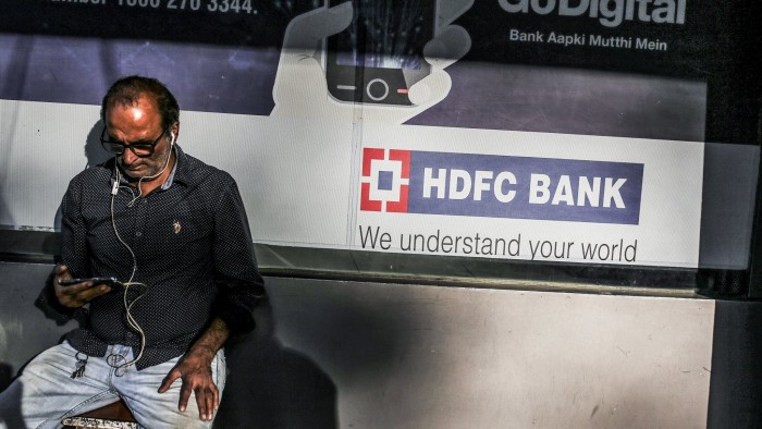 A man looks at a mobile phone as he sits near a HDFC bank Ltd. branch in Mumbai, India, on Saturday, Jan. 27, 2018. India's economy is expected to grow at 6.75 percent this year on the back of a recovery in second half of the year, Chief Economic Adviser Arvind Subramanian said in the Economic Survey presented in Parliament on Nov. 29. Photographer: Dhiraj Singh/Bloomberg