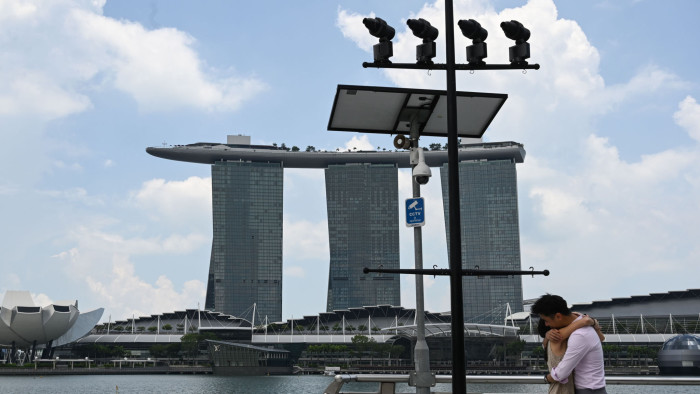 A couple hugs under a closed circuit television (CCTV) surveillance camera in Marina Bay in Singapore on April 2, 2020, as the government slowly tightens restrictions to combat the spread of the COVID-19 novel coronavirus. (Photo by Roslan RAHMAN / AFP) (Photo by ROSLAN RAHMAN/AFP via Getty Images)