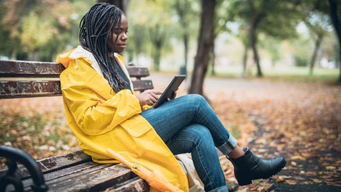 Young woman with yellow raincoat enjoying in the autumn park, using digital tablet