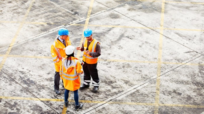 High angle shot of three workers talking together while standing on a commercial dock