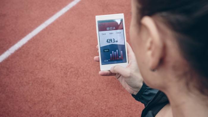 Spain, Asturias, Back view of brunette woman looking smartphone with training data on screen over running track background