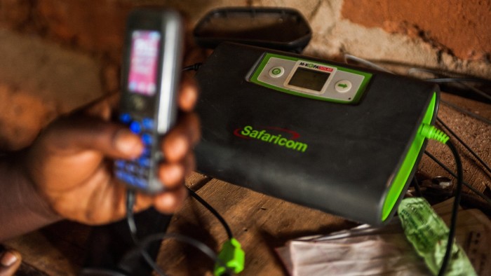 Rebecca Wambua, holds a mobile phone charging at a Safaricom electrical unit using M-Kopa solar technology in Ndela village, Machakos country, Kenya, on Wednesday, July 22, 2015. Customers agree to pay for the solar panel with regular instalments which M-Kopa, a Nairobi-based provider of solar-lighting systems, then monitors for payments that are made using a mobile-phone money-transfer service. Photographer: Waldo Swiegers/Bloomberg
