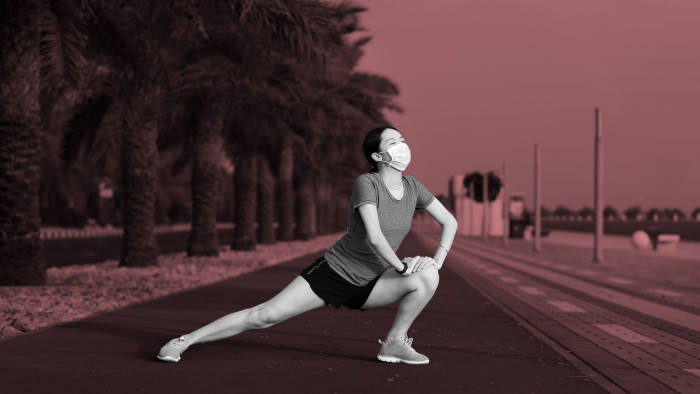Asian woman exercising and stretching while wearing protective surgical mask to warm up before fitness workout outdoors