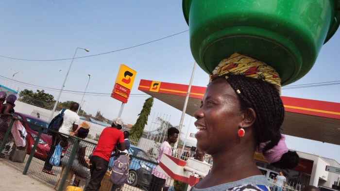 A fruit vendor carries her wares past a petrol station of Sonangol, the national fuel society of Angola, in Luanda on November 13, 2018. - One year after the election of President Joao Lourenco, the oil-rich nation is still waiting for the economic &quot;miracle&quot; that he promised on the campaign trail. In a country scarred by prolonged war -- and where the economic benefits of an oil-fuelled boom have not always trickled down to the mass population -- entrenched poverty remains the norm for nearly half the population. (Photo by Rodger BOSCH / AFP) (Photo credit should read RODGER BOSCH/AFP/Getty Images)