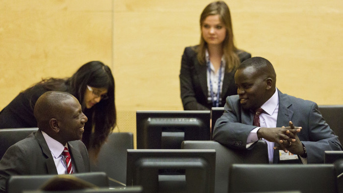 William Ruto, left, speaks to Joshua Sang, right, in the courtroom before their trial begins