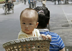 Beijing, CHINA: A baby is carried in a basket on his mothers back on a street in Beijing, 07 June 2007. Introduced in 1978 amid fears of runaway population growth, China's one-child policy limits urban families to a single child while allowing exceptions for rural and ethnic minority families but has been blamed for fueling a black market for babies with the theft and trafficking of infants a major problem in China among families who are eager to have another child, particularly males, who are prized as a future source of support for aging parents. AFP PHOTO/Peter PARKS. (Photo credit should read PETER PARKS/AFP/Getty Images)