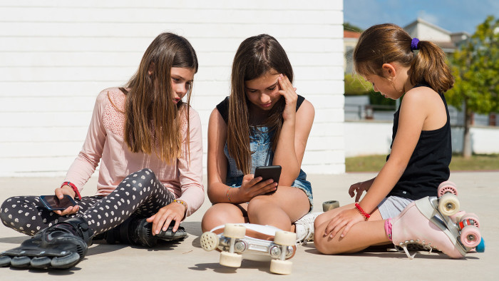 three girls pause from rollerskating to play on the phone