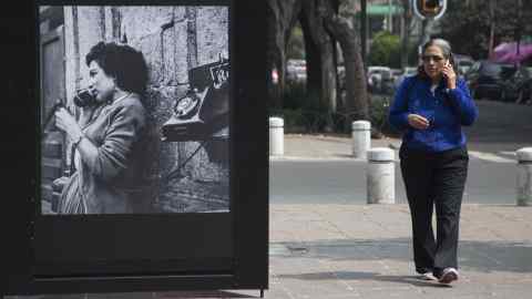 A woman talks on her phone as she walks next to a photo of the "Roma Photo Exhibition" on Alvaro Obregon Avenue, in Mexico City, Saturday, Feb. 9, 2019. As part of the activities organized in the framework of the Oscars ceremony and due to the nomination of the film ROMA by Mexican Director Alfonso Cuaron, Mexico City‚Äôs government inaugurated the "Roma Photo Exhibit" which are a series of photographs of the Roma neighborhood through time. (AP Photo/Christian Palma)