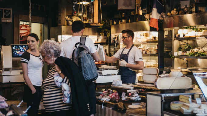 London, UK - September 17, 2018: Seller and customers inside charcuterie and cheese stand in Borough Market, one of the largest and oldest food markets in London.