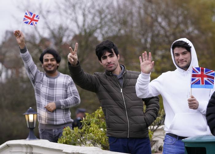 Afghan refugees waving UK flag by the roadside