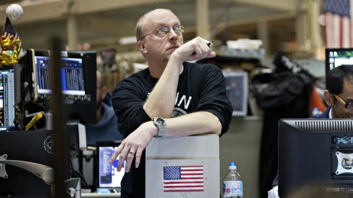 A trader looks up to watch screens while leaning on a computer with a US flag stuck to it