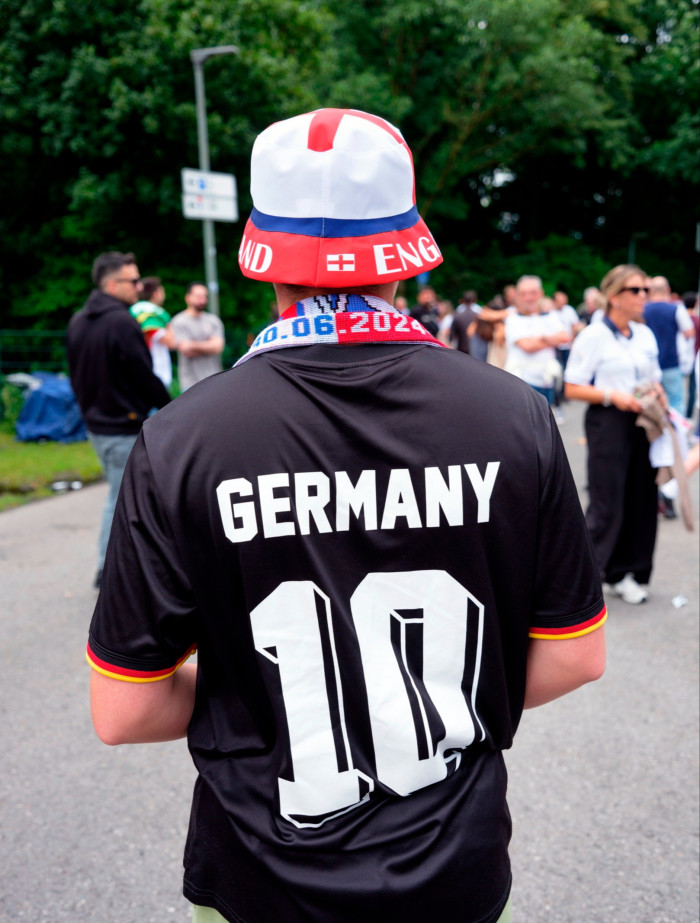 A figure, seen from behind, wears a black football shirt that says Germany 10 and a bucket hat with the word England on the rim