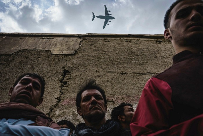 A military transport plane flies over a group of men who had gathered at the site of a US drone strike in Kabul, August 30
