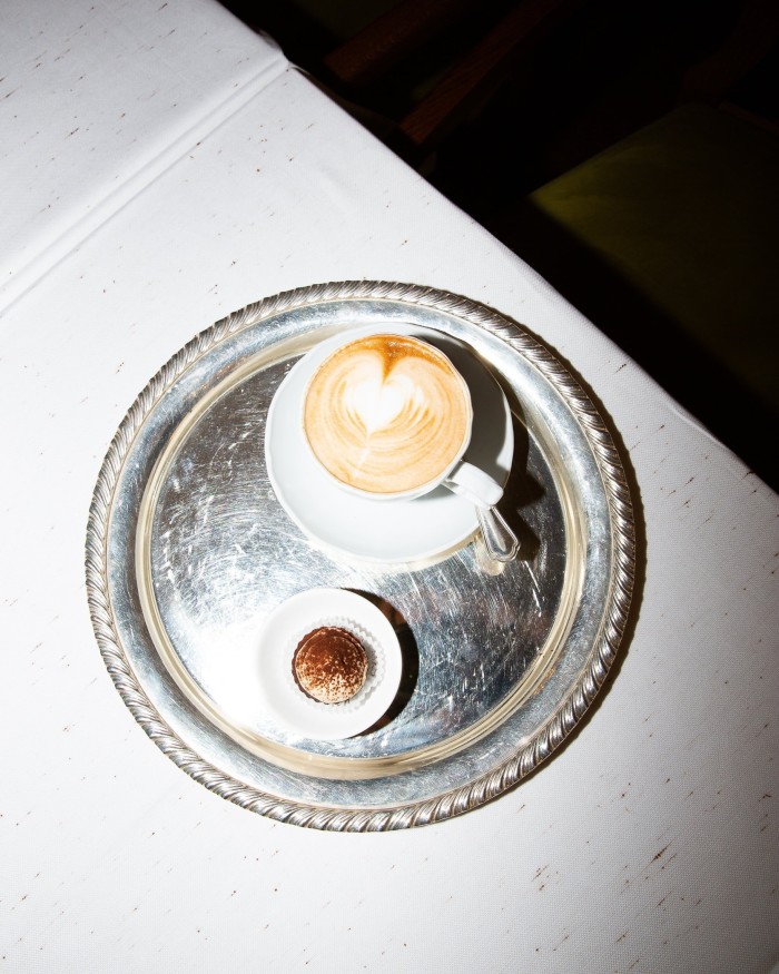 An espresso on a small circular silver tray alongside a bite-sized