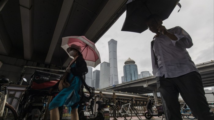 Pedestrians carry umbrellas while walking through the Guomao central business district in Beijing