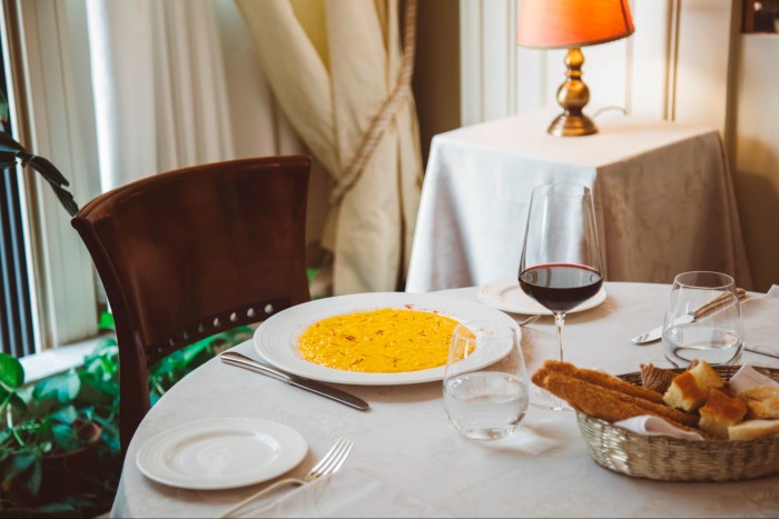 A plate of Milanese saffron risotto and a glass of red wine on set table at Boeucc