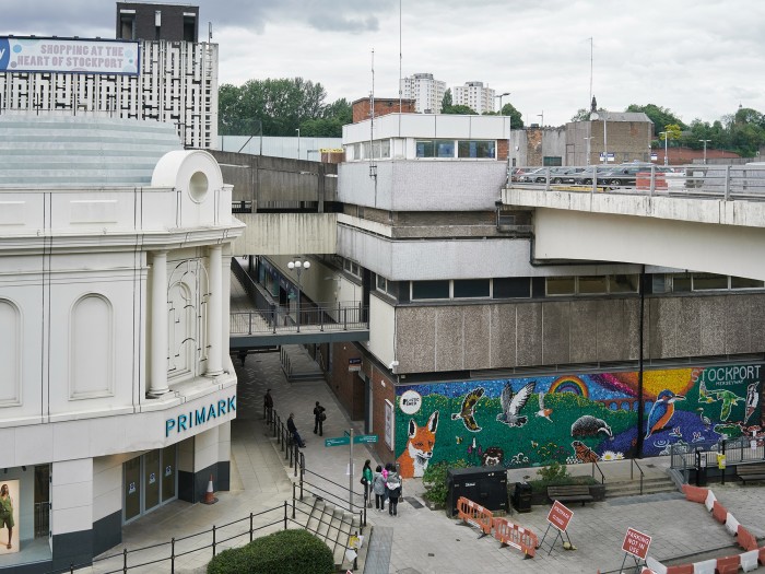 Aerial view showing a 1970s building with a colourful mosaic on the outside wall. Work is being done to renew the paving outside