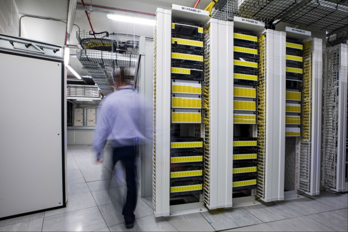 An employee walks past racks of panels inside a communications room at an office 