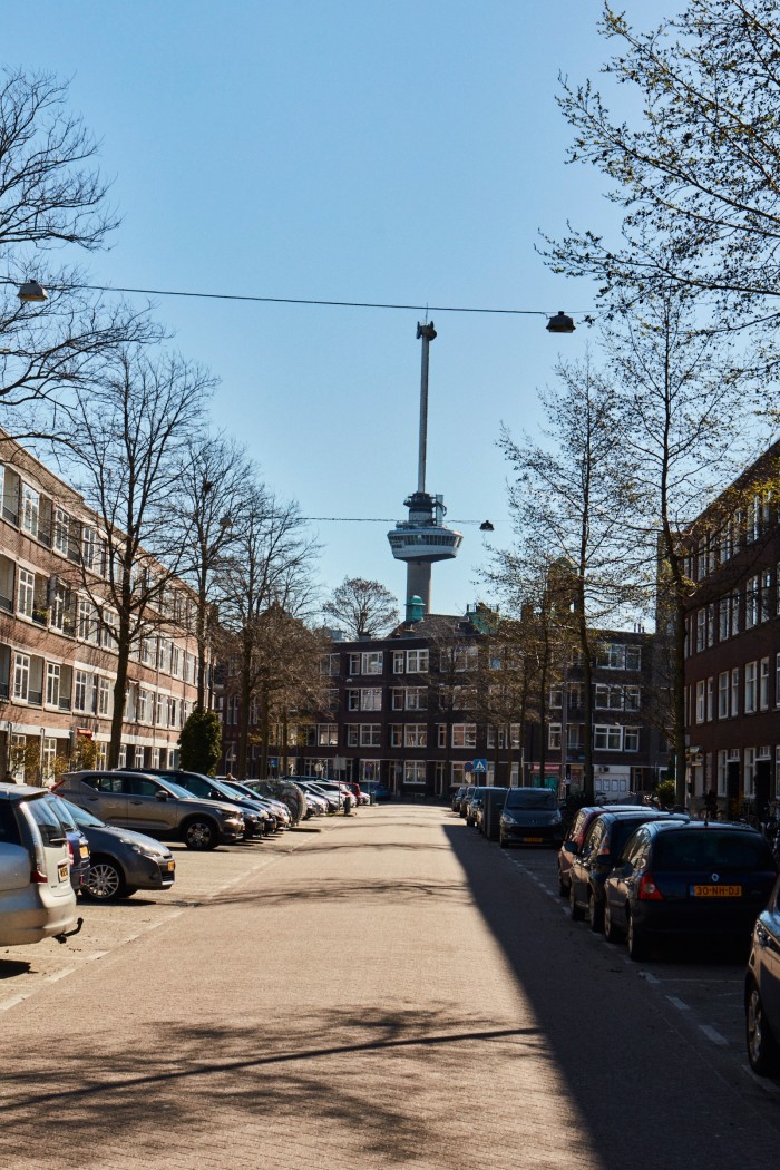 A residential street with the top half of the Rotterdam Euromast in the distance, against a blue sky