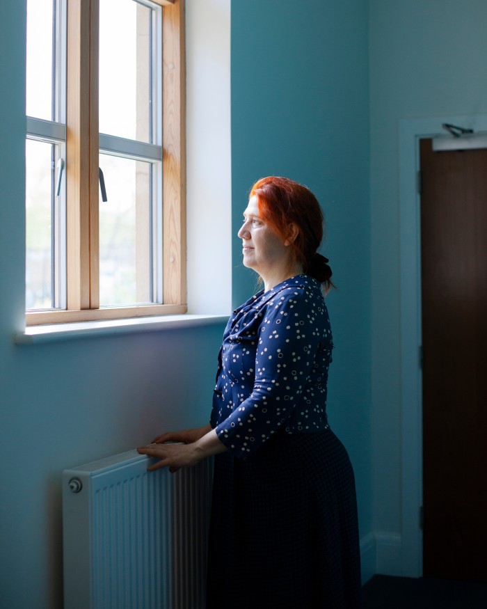 Alison East rests her hands on a radiator as she looks out of a window