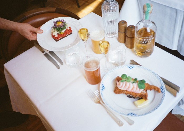 Two of Møntergade’s smørrebrød – classic beef tartare with horse radish, pickles and egg yolk (left) and fried plaice with mayonnaise and shrimps – on plates on a set table