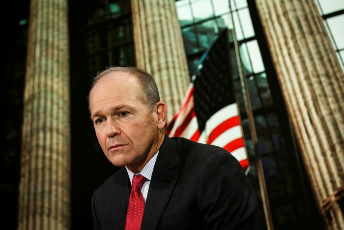 Boeing’s Dave Calhoun, in a dark suit, white shirt and red tie, looking pensive in front of a US flag