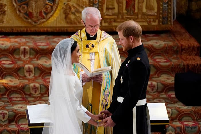 Welby standing behind Markle and Prince Harry, who are facing each other and holding hands