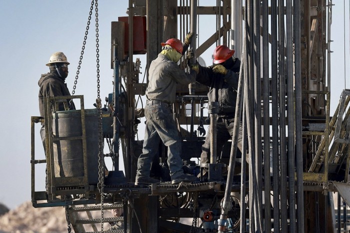 Workers place a pipe into the ground on an oil drilling rig in the Permian Basin