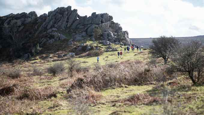 People running along moorland next to a tor