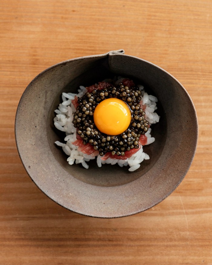 Tuna on rice with quail egg and caviar in a small brown-metal bowl