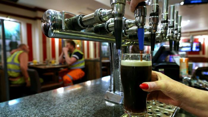 A barmaid pulls a pint of Guinness inside a pub in London